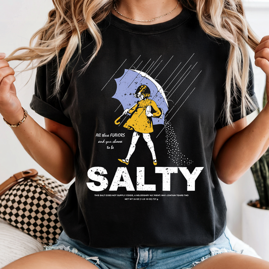 Woman wearing a black t-shirt with a graphic design and the word 'SALTY' indoors.